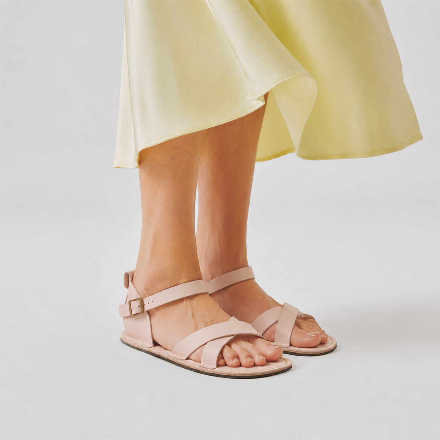 Crema | Close-up of model wearing flat sandals with an ankle strap and buckle, shown against a plain background