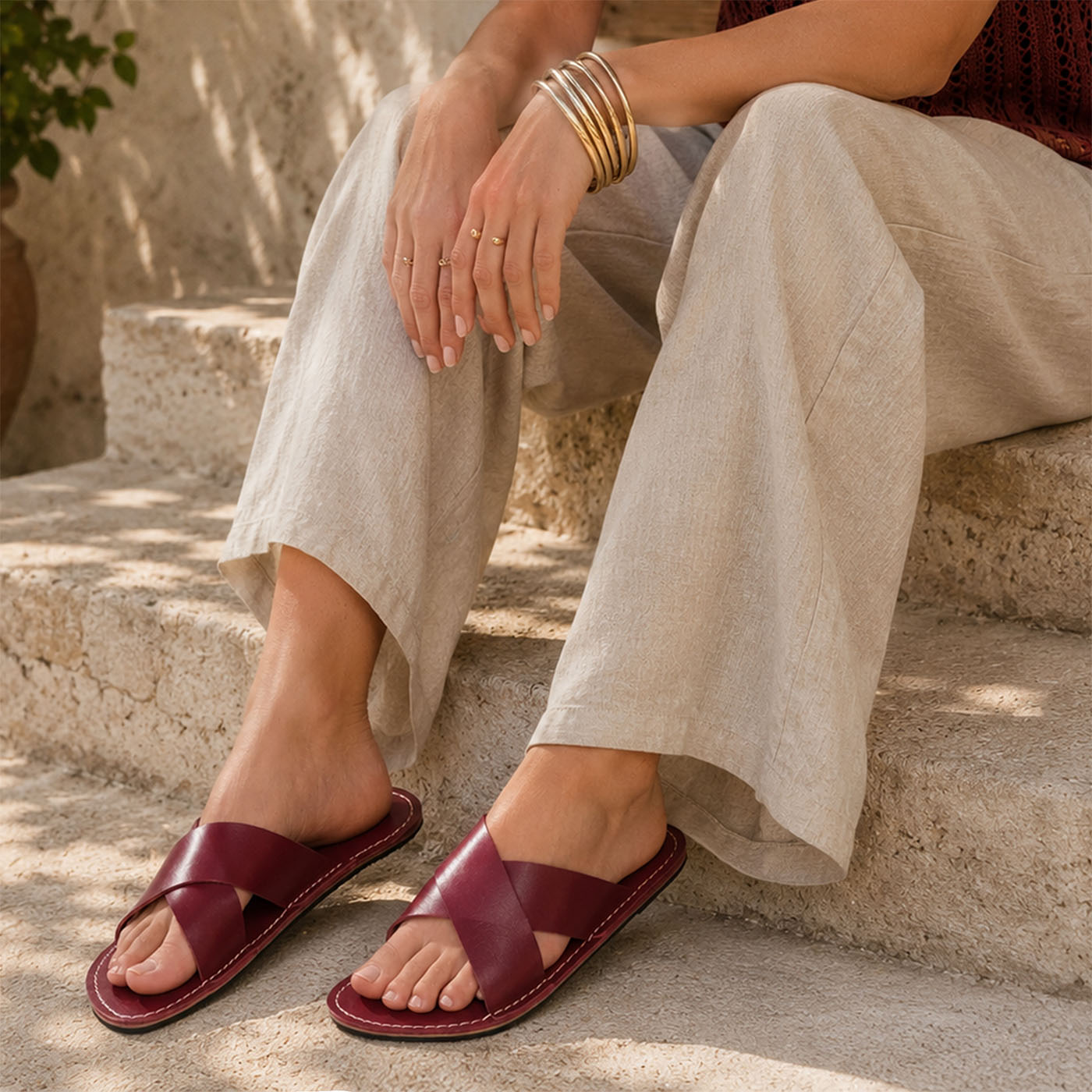 Marsala | Close-up of model wearing gray pants and red wine colored-leather flat sandals sitting on concrete steps