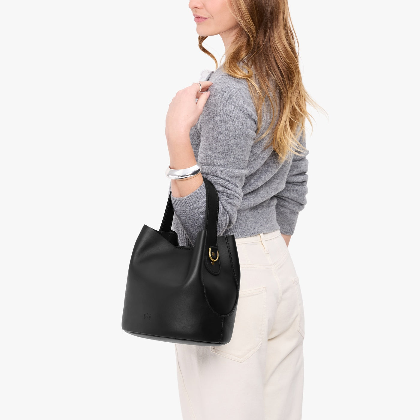 Black*Large | Model carrying symmetrical bucket bag with handle, latch closure, and removable crossbody strap