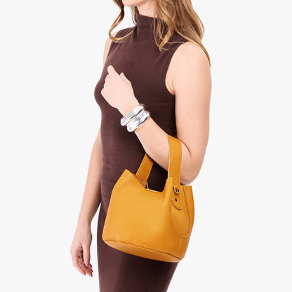 Sunshine*Small | Model carrying symmetrical bucket bag with handle, latch closure, and removable crossbody strap
