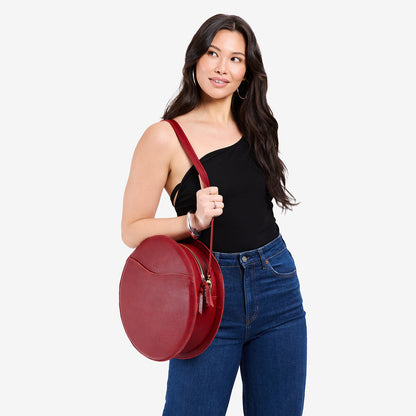 Chili Red | Model carrying large circle shaped leather bag with top zipper and carrying strap