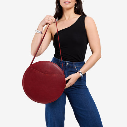 Chili Red | Model holding large circle shaped leather bag with top zipper and carrying strap