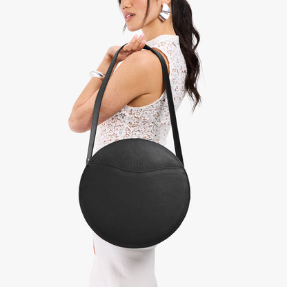 Pebbled--black | Model carrying large circle shaped leather bag with top zipper and carrying strap