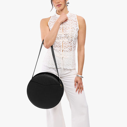 Pebbled--black | Model carrying large circle shaped leather bag with top zipper and carrying strap
