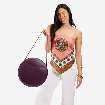 Plum | Model carrying large circle shaped leather bag with top zipper and carrying strap