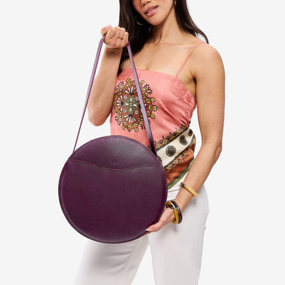 Plum | Model holding large circle shaped leather bag with top zipper and carrying strap