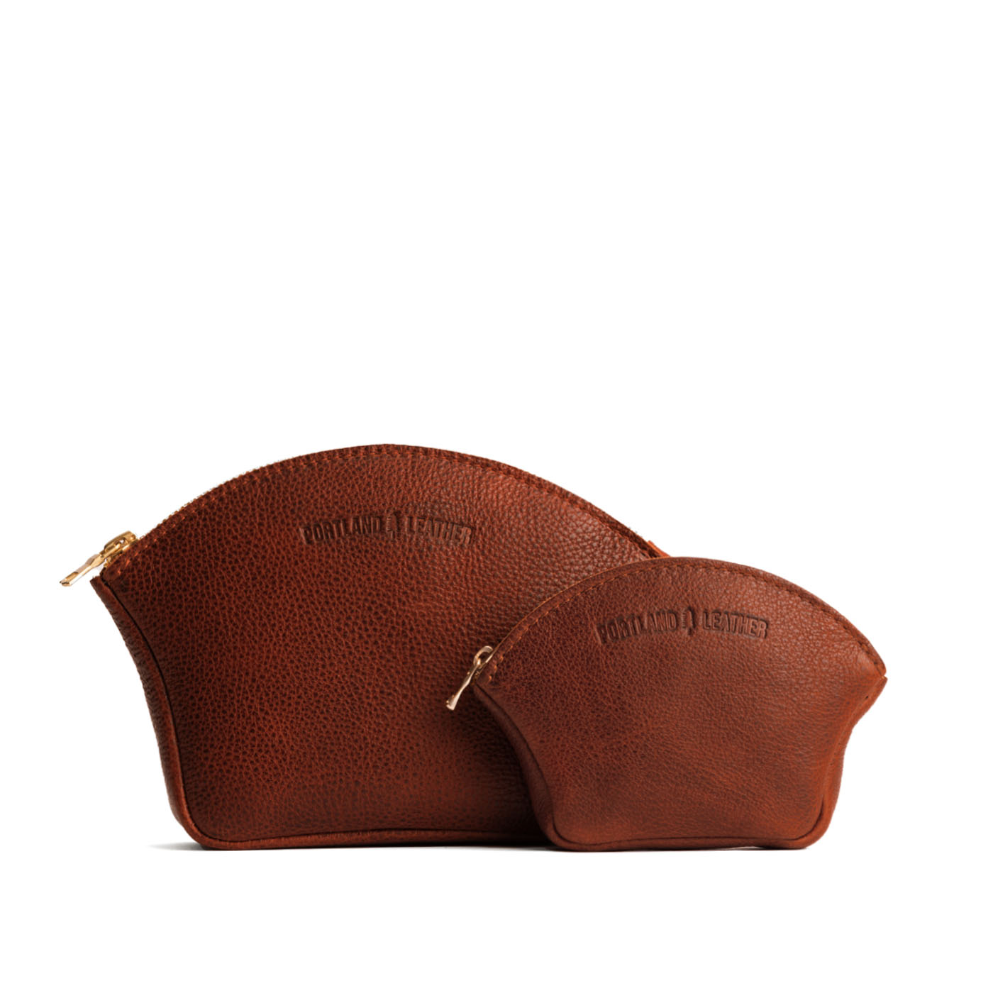 Nutmeg | Comparison shot of small and large seashell shaped leather makeup bags with curved top zipper and flat bottom