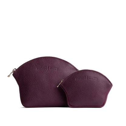 Plum | Comparison shot of small and large seashell shaped leather makeup bags with curved top zipper and flat bottom