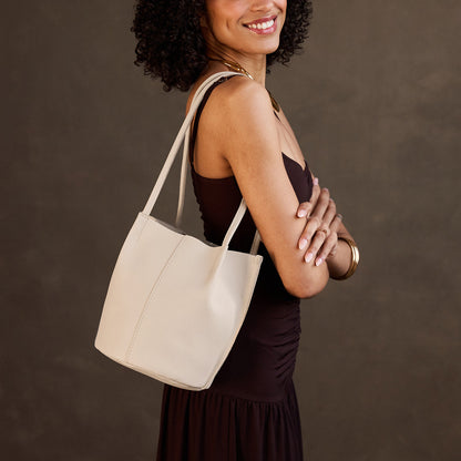 Bone*Small | Model wearing sleeveless dark brown dress carrying petite bucket shaped tote bag with matching leather handles against dark grey background