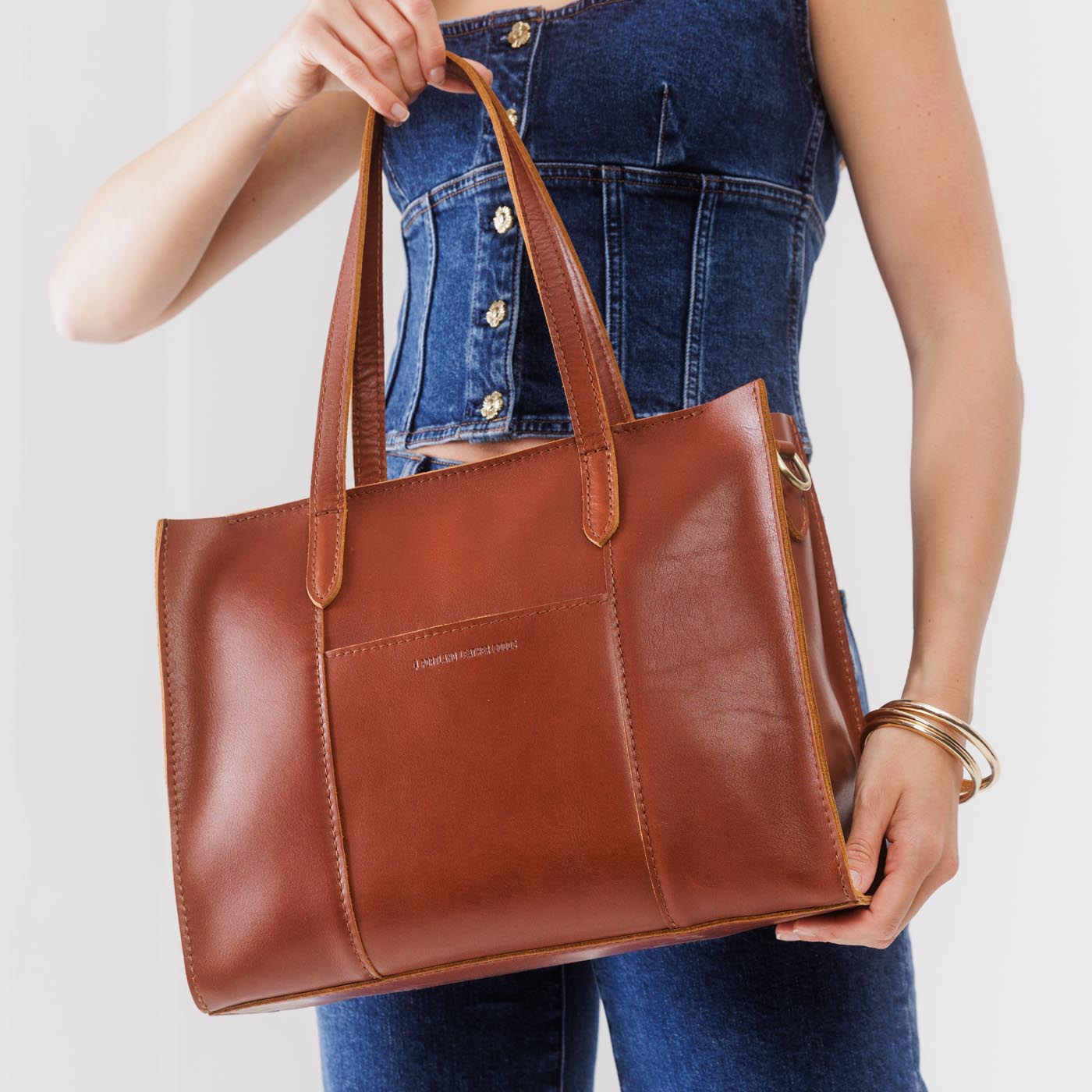 Chestnut*East/West | Model holding structured wide tote bag with overlapping panels and crossbody strap
