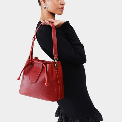 Chili Red*Large | Model holding symmetrical leather bag with leather drawstring closure and adjustable shoulder strap
