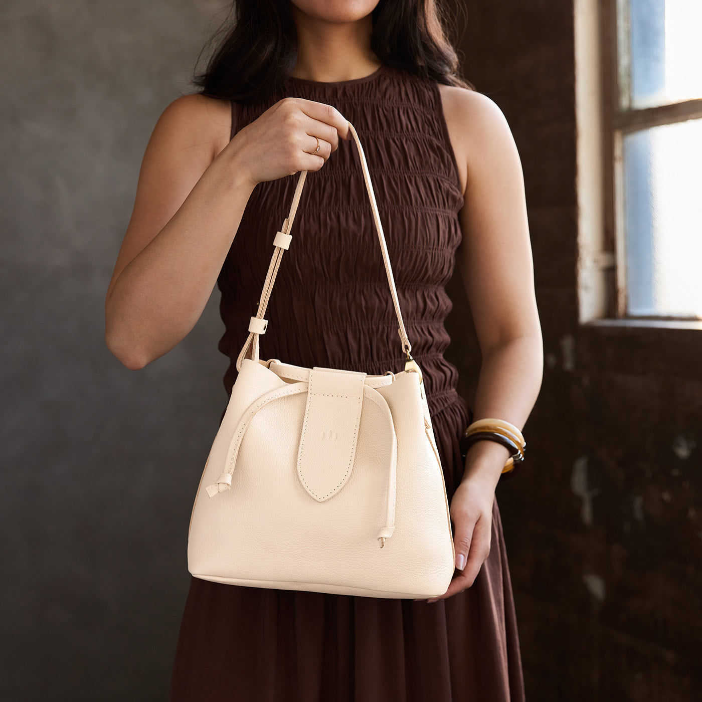Pebbled Bone*Large | Model holding symmetrical leather bag with leather drawstring closure and adjustable shoulder strap