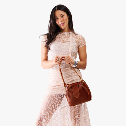 Nutmeg*Small | Model holding symmetrical leather bag with leather drawstring closure and adjustable shoulder strap