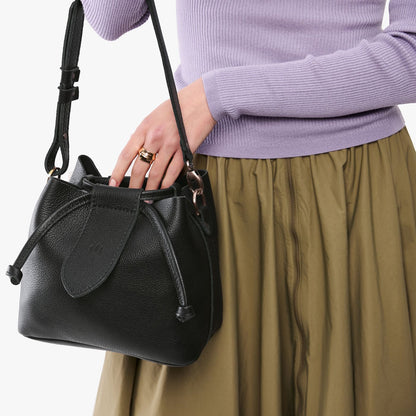 Pebbled--black*Small | Model holding symmetrical leather bag with leather drawstring closure and adjustable shoulder strap
