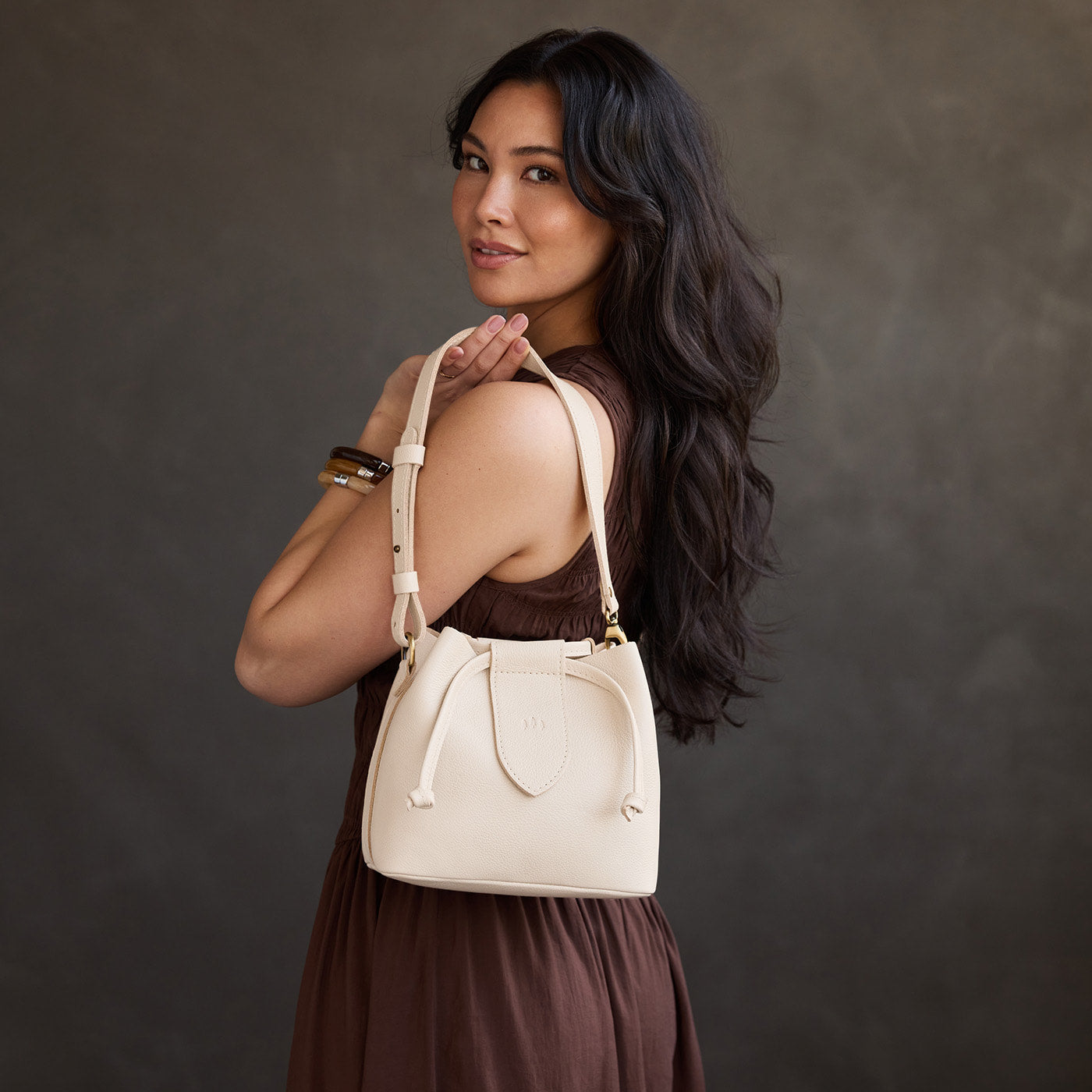 Pebbled Bone*Small | Model holding symmetrical leather bag with leather drawstring closure and adjustable shoulder strap