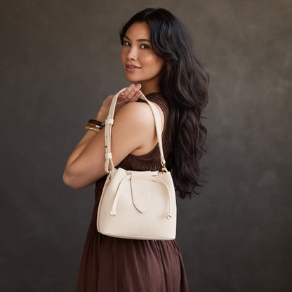 Pebbled Bone*Small | Model holding symmetrical leather bag with leather drawstring closure and adjustable shoulder strap