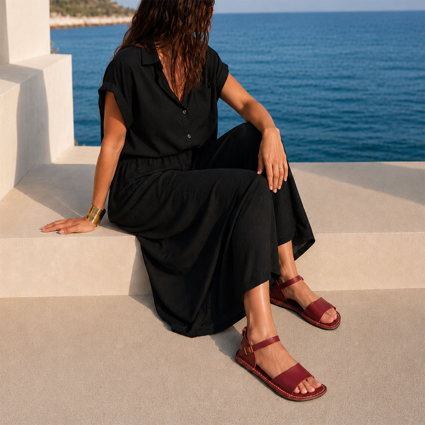 Marsala | Close-up of a person wearing colorful dress and red flat sandals with an ankle strap and buckle, shown against a plain background.