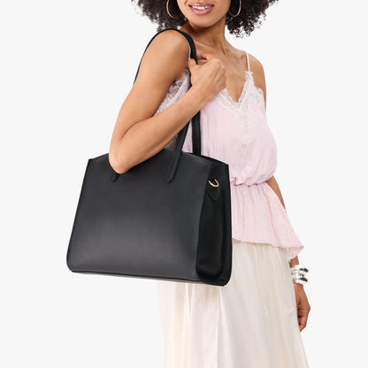 Black*Large | Model carrying leather tote bag with handles, adjustable crossbody strap, and two back pockets
