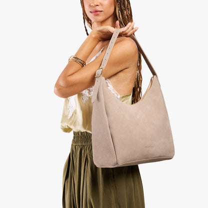 Taupe*Large | Model holding u-shaped, flat-bottomed leather shoulder bag with adjustable strap