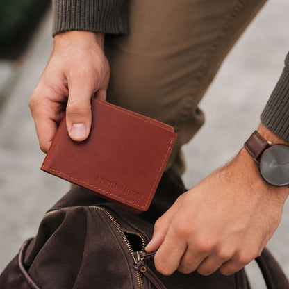 Marrone | A bifold wallet being put into a backpack