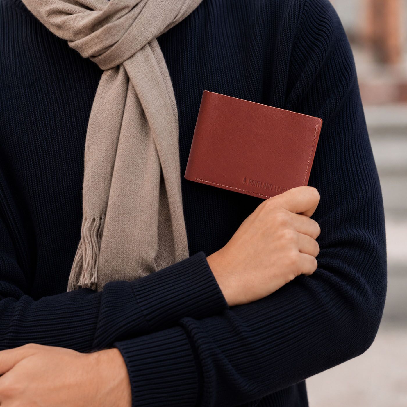 Marrone | A person wearing a sweater holding a bifold wallet