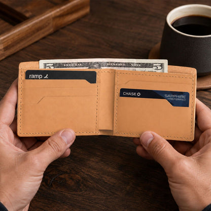 Naturale | A leather bifold wallet held open by two hands over a dark wooden table, with cash and cards visible inside.