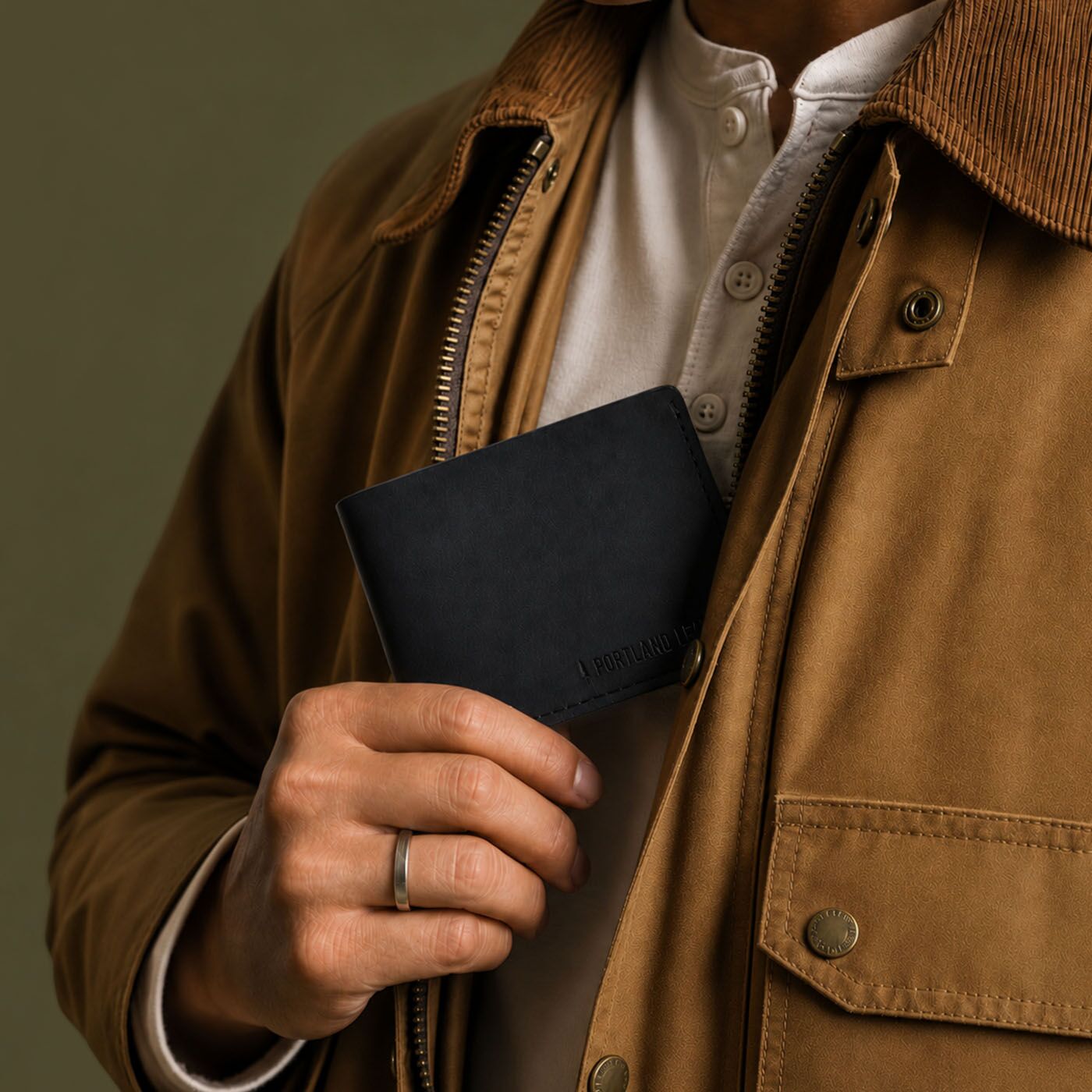 Nero | A close-up of a person wearing a brown corduroy jacket over a white shirt, holding a leather bifold wallet against their chest.