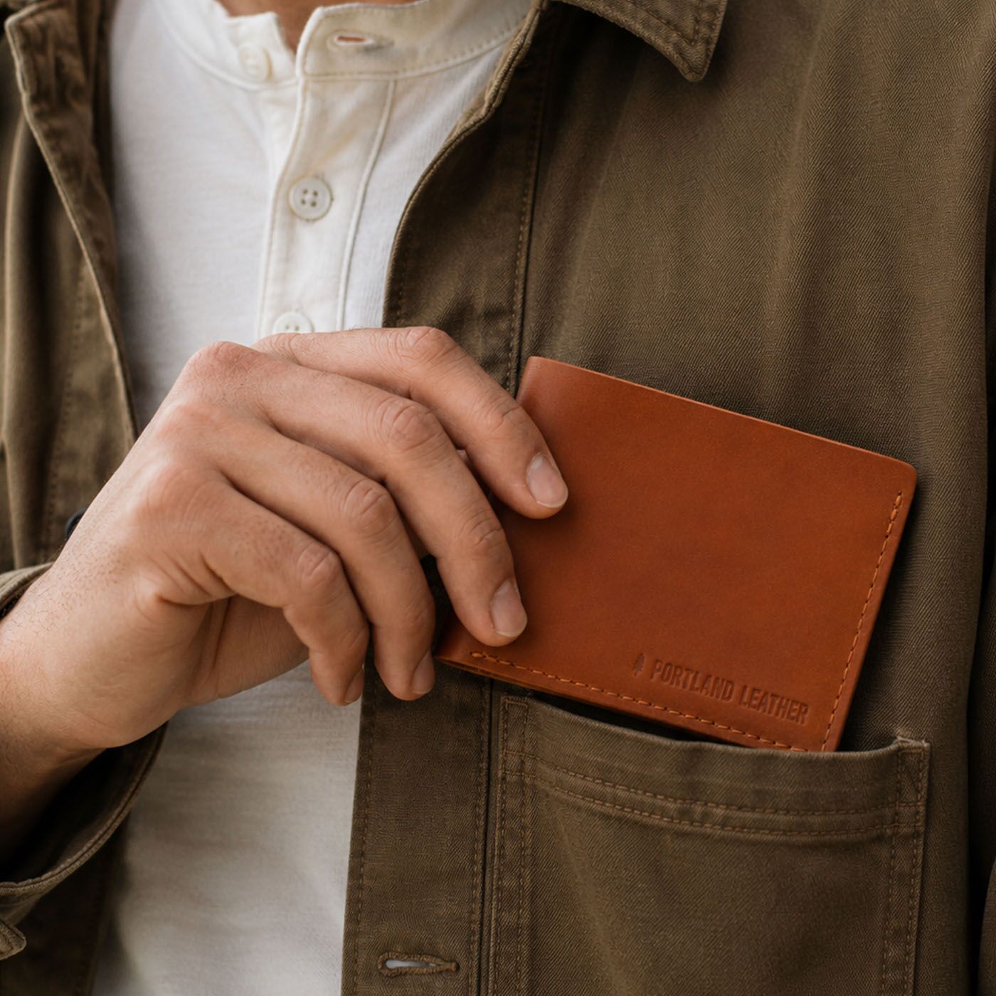 Toscano | A close-up of a person holding a brown leather card holder in their hand and placing it into the chest pocket. The card holder has 'PORTLAND LEATHER' debossed on the bottom right corner.