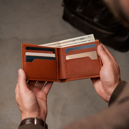 Toscano | A person holds an open leather bifold wallet with multiple card slots and cash