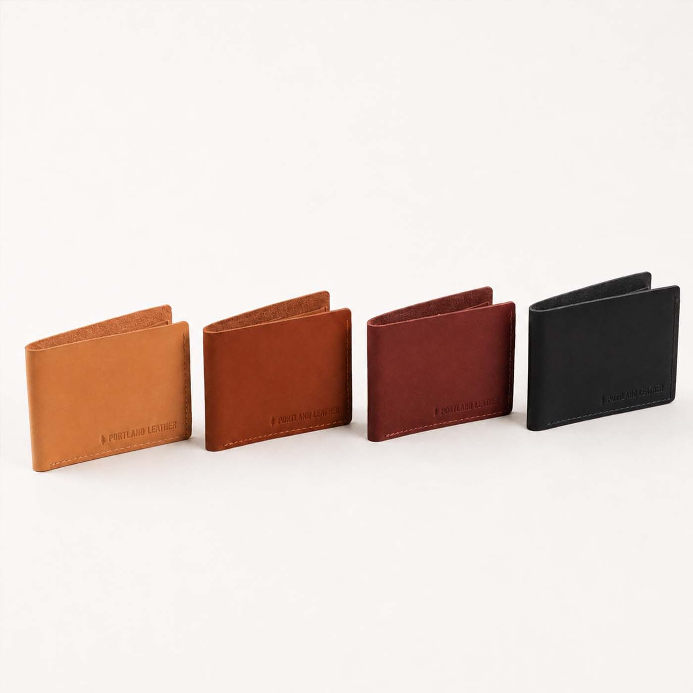 Toscano | Four leather bifold wallets lined up in a row on a clean white background. Each wallet features a minimalist bi-fold design with a debossed logo near the bottom edge.