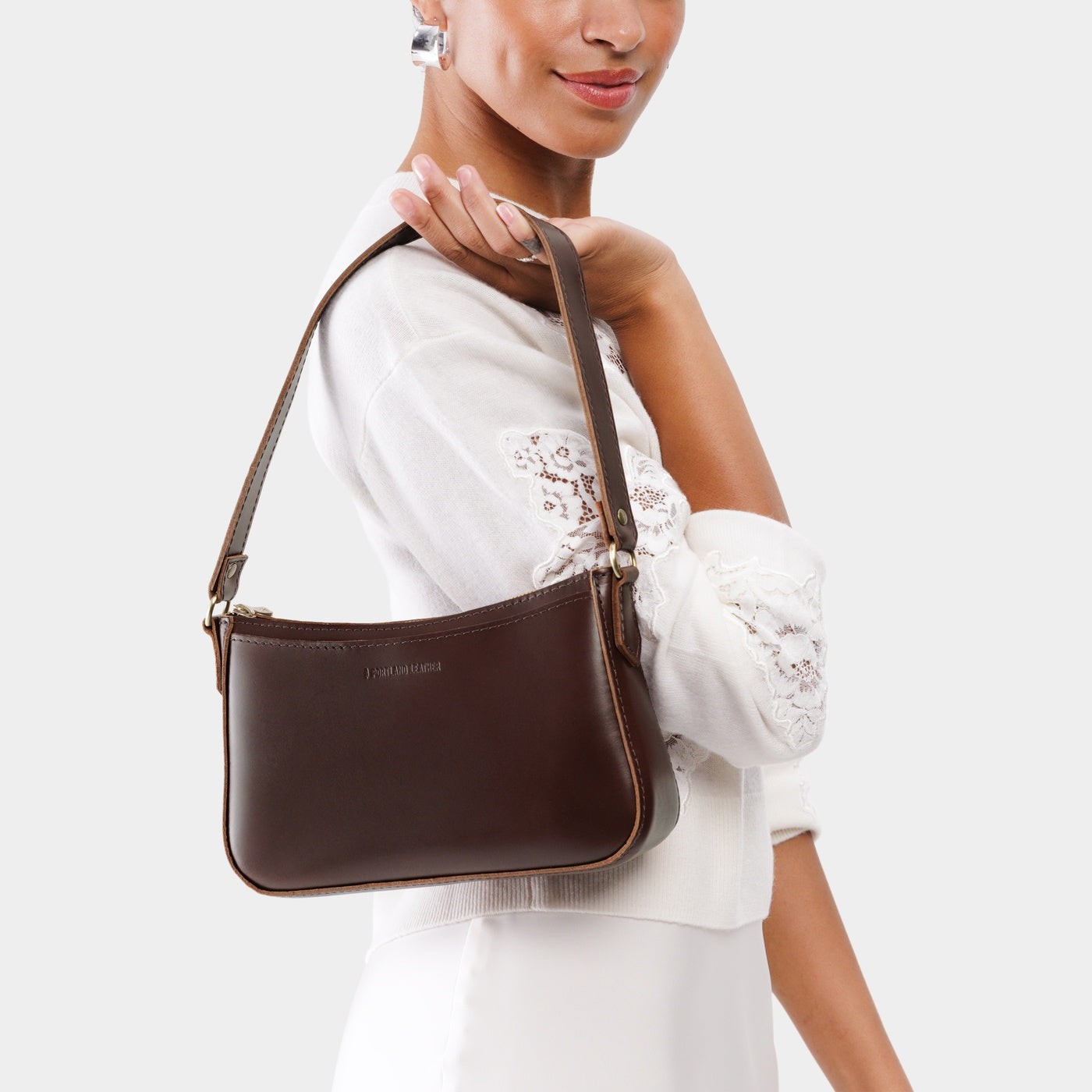 Chocolate Brown*Small | Model holding petite bean shaped shoulder bag with a zipper closure