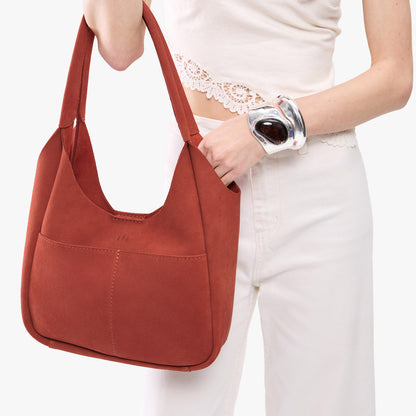 Cinnabar*Large | A model holding a u-shaped, flat-bottomed leather shoulder bag with two outside pockets