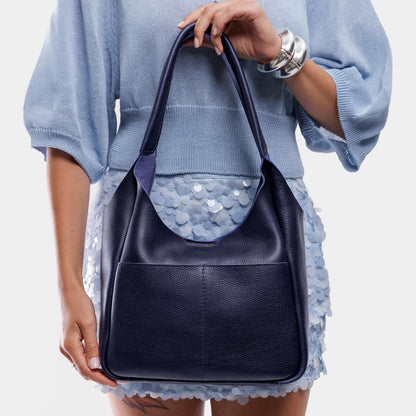 Cobalt*Large | A model holding a u-shaped, flat-bottomed leather shoulder bag with two outside pockets