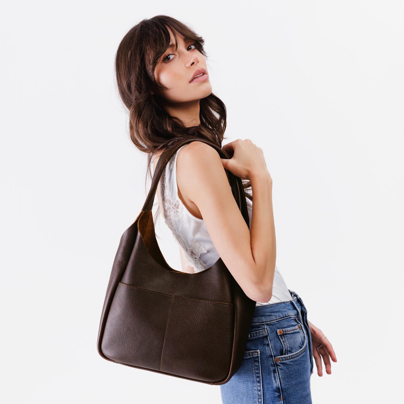 Coldbrew*Large | A model holding a u-shaped, flat-bottomed leather shoulder bag with two outside pockets