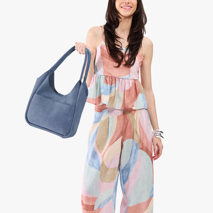 Denim*Large | A model holding a u-shaped, flat-bottomed leather shoulder bag with two outside pockets