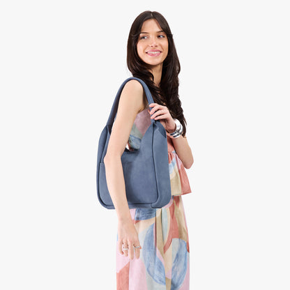 Denim*Large | A model holding a u-shaped, flat-bottomed leather shoulder bag with two outside pockets