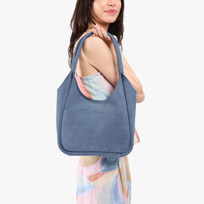 Denim*Large | A model holding a u-shaped, flat-bottomed leather shoulder bag with two outside pockets