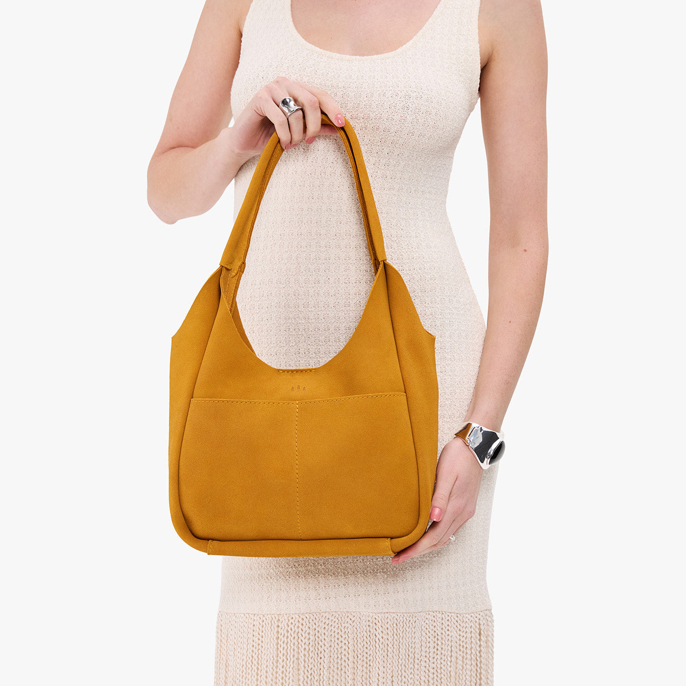 Dijon*Large | A model holding a u-shaped, flat-bottomed leather shoulder bag with two outside pocketsv