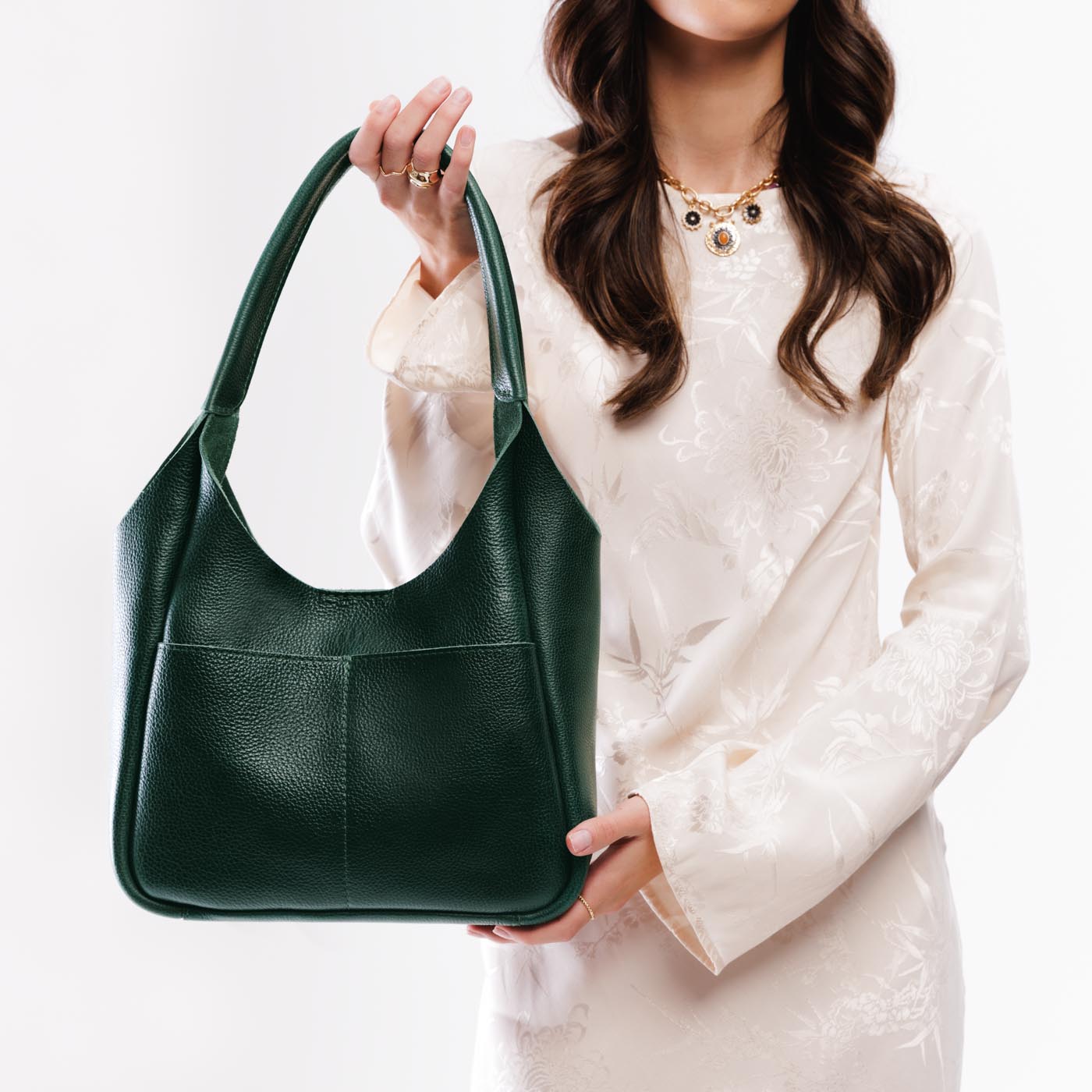 Forest Green*Large | A model holding a u-shaped, flat-bottomed leather shoulder bag with two outside pockets