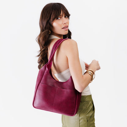 Orchid*Large | A model holding a u-shaped, flat-bottomed leather shoulder bag with two outside pockets