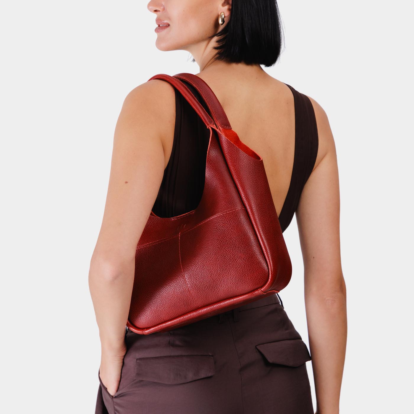 Chili Red*Medium | A model holding a u-shaped, flat-bottomed leather shoulder bag with two outside pockets
