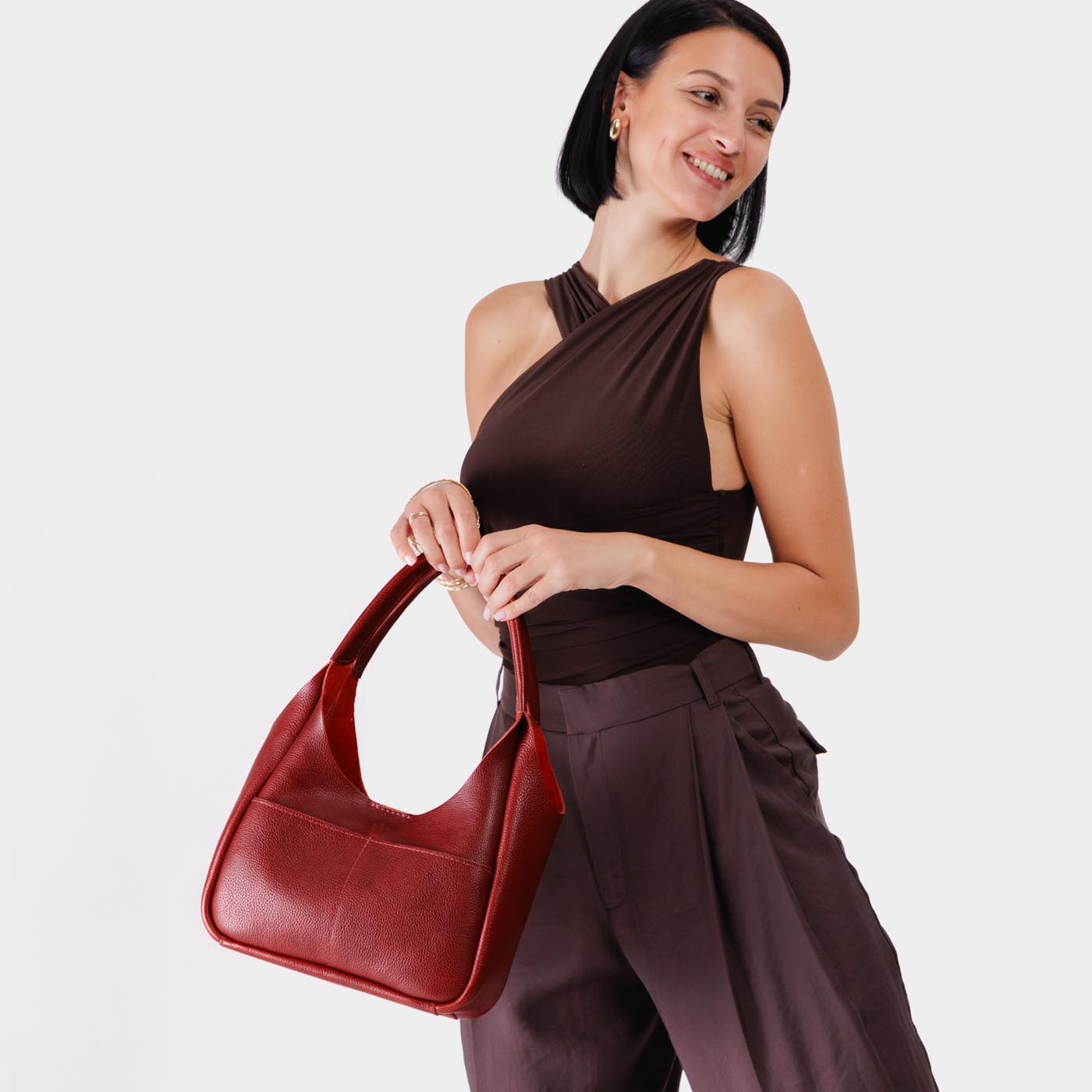 Chili Red*Medium | A model holding a u-shaped, flat-bottomed leather shoulder bag with two outside pockets
