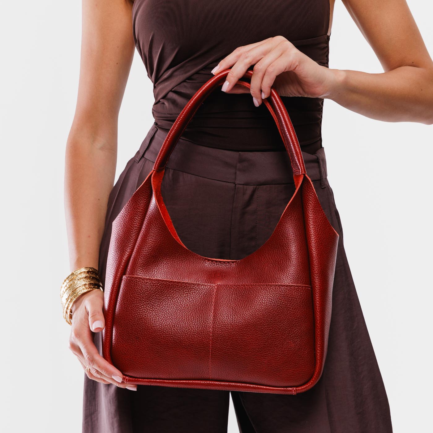 Chili Red*Medium | A model holding a u-shaped, flat-bottomed leather shoulder bag with two outside pockets
