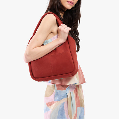 Cinnabar*Medium | A model holding a u-shaped, flat-bottomed leather shoulder bag with two outside pockets