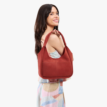 Cinnabar*Medium | A model holding a u-shaped, flat-bottomed leather shoulder bag with two outside pockets