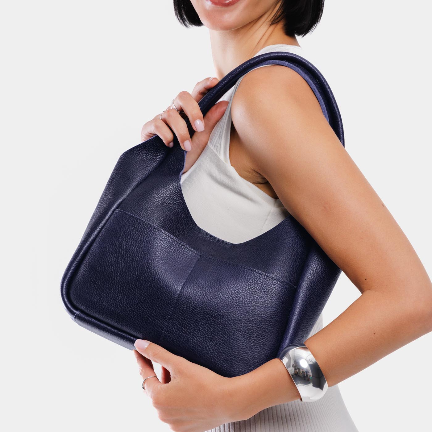 Cobalt*Medium | A model holding a u-shaped, flat-bottomed leather shoulder bag with two outside pockets