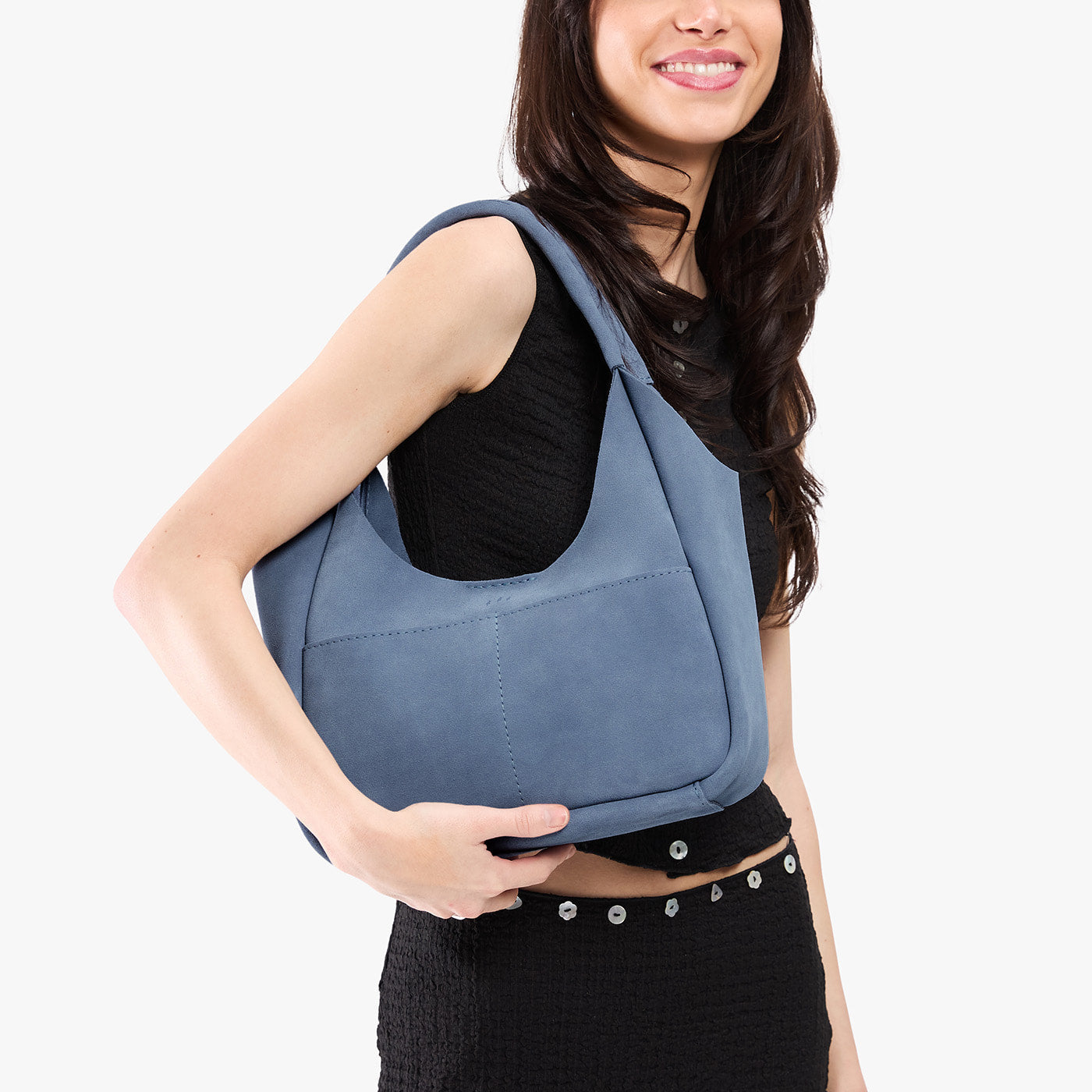 Denim*Medium | A model holding a u-shaped, flat-bottomed leather shoulder bag with two outside pockets