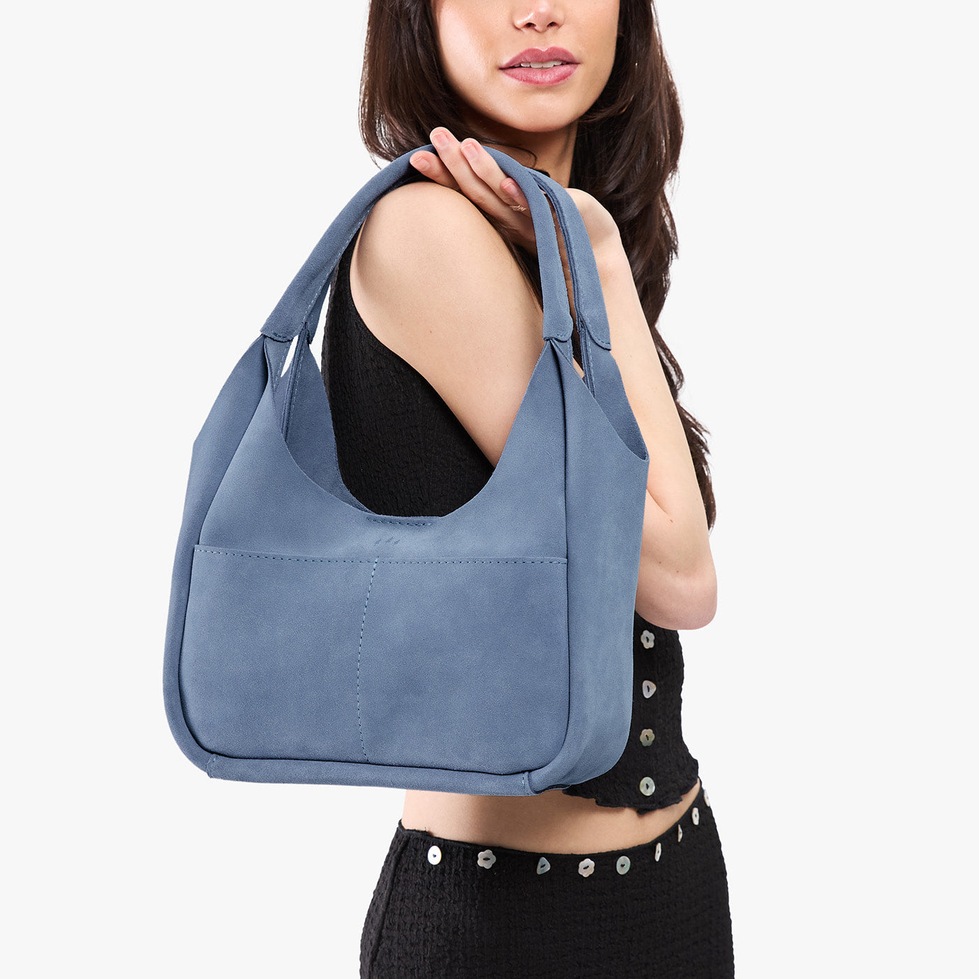Denim*Medium | A model holding a u-shaped, flat-bottomed leather shoulder bag with two outside pockets