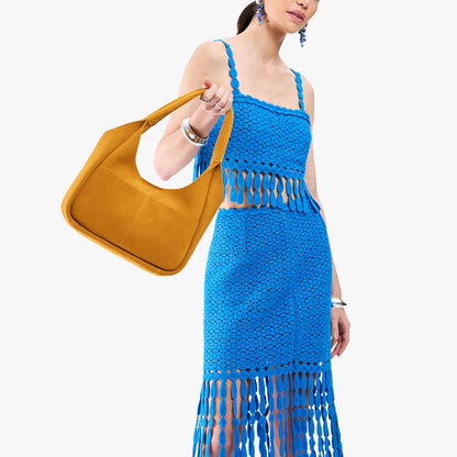Dijon*Medium | A model holding a u-shaped, flat-bottomed leather shoulder bag with two outside pockets