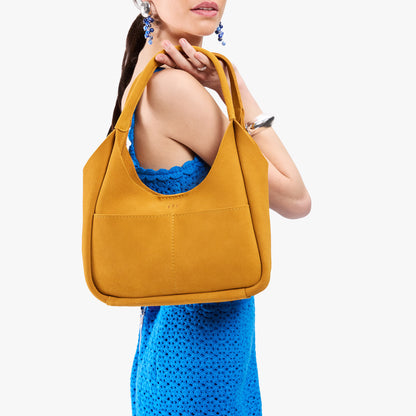 Dijon*Medium | A model holding a u-shaped, flat-bottomed leather shoulder bag with two outside pockets